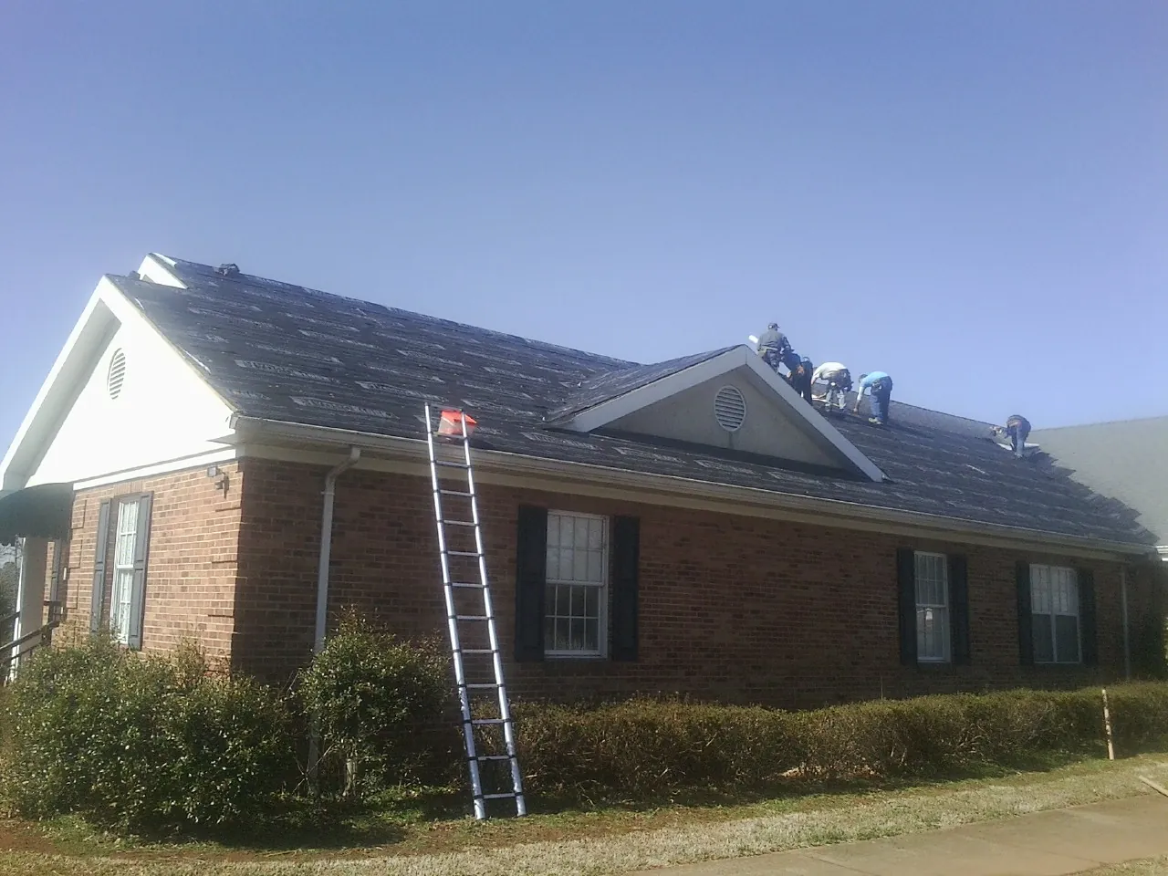 Crew tearing shingles off a brick ranch roof with a ladder set — Emergency Roof Repair work by our crew in New Freedom