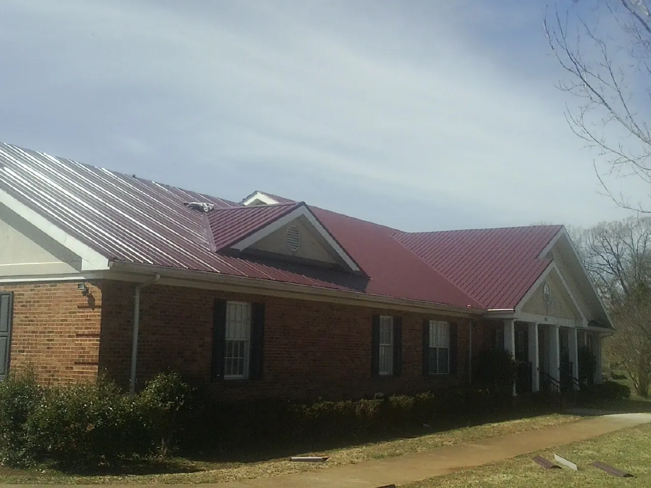 Red metal roof with gabled entries on a long brick building, from a Hail Damage Roof Repair job in New Freedom