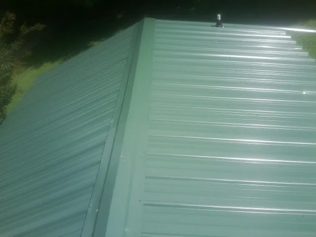 New green metal panels meeting at the ridge of a roof — Flat Roof Repair work by our crew in New Freedom