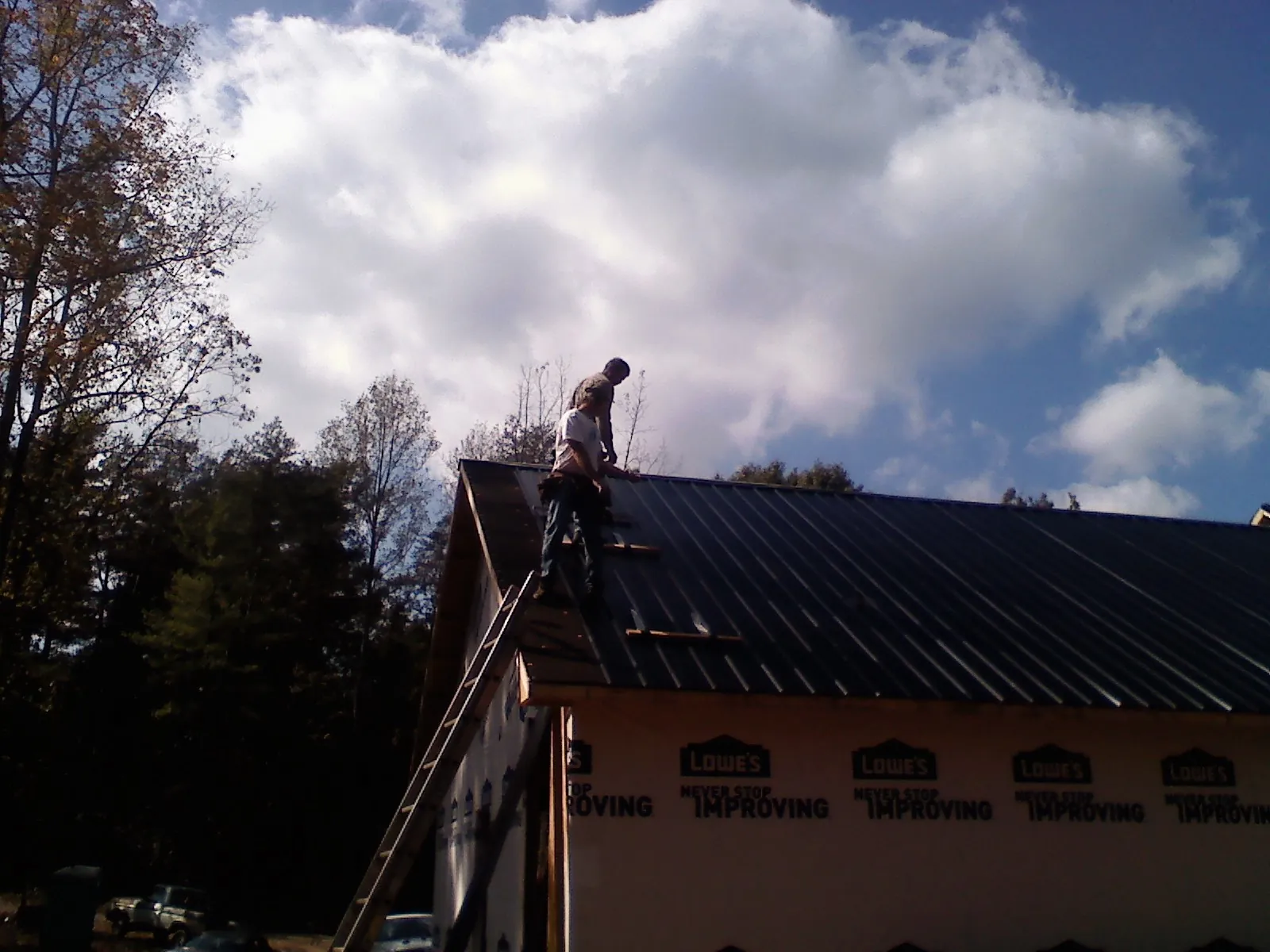 Roofer fastening dark metal panels high against a cloudy sky, from a Roof Inspection job in New Freedom