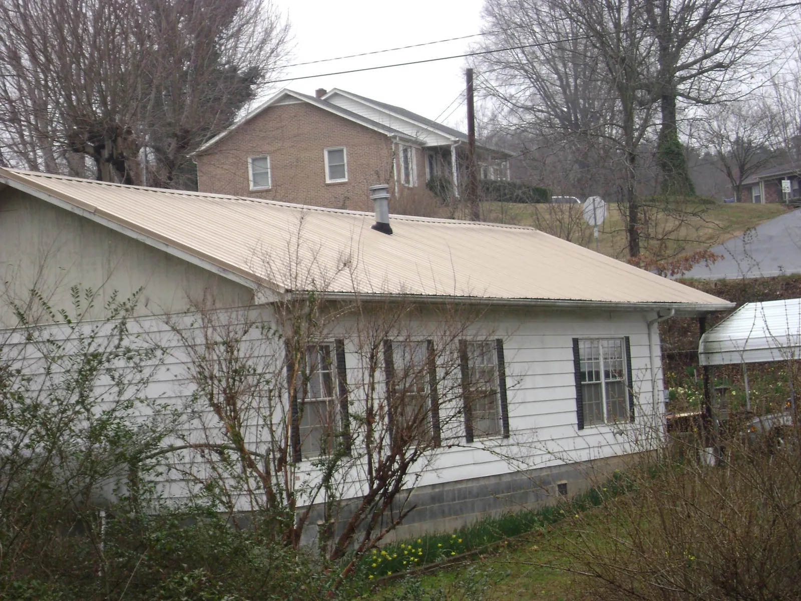 Tan metal roof on a white sided house set into a hillside — Commercial Roofing by Roofing Brothers in New Freedom